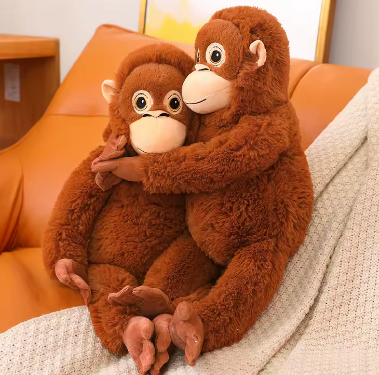 Two brown plush monkeys hugging on a couch.